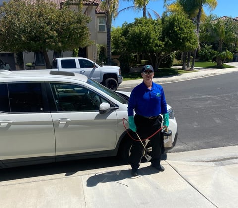 Service worker in blue uniform standing next to white car during driveway service call