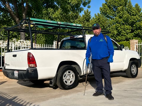 Service worker in blue shirt standing beside white pickup truck with roof rack and ladder